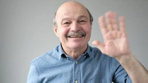 Pensioner waves hand in hello gesture while smiling cheerfully. Stock Photos