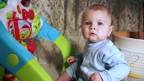 Pensive baby sits near developing toy and looks at camera 스톡 동영상 169437941