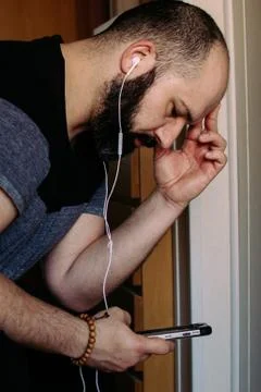 Pensive bearded man looking at mobile phone while listening to music on headp Stock Photos