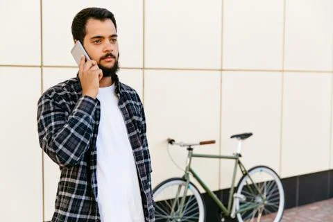 Pensive bearded man talking on mobile phone, standing outdoors. Stock Photos