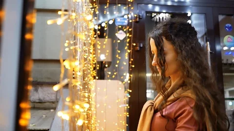 Pensive beautiful young woman is sad near cafe on background of orange garlands Stock Footage
