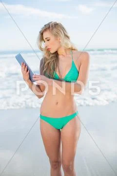 Pensive blonde model in green bikini using a tablet pc Stock Photos