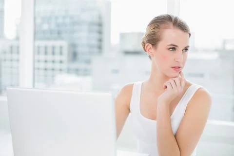 Pensive blonde using her laptop Stock Photos