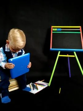 Pensive boy in a blue suit boy reads something on a blue tablet Stock Photos