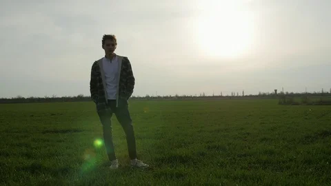 Pensive boy standing in the green grass field at sunset Видео 106314844