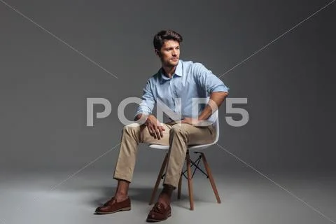 Pensive brunette man in blue shirt sitting on the chair Stock Photos