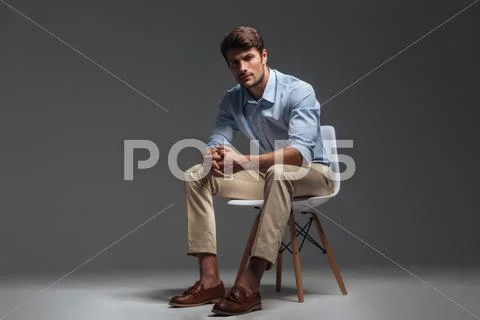 Pensive brunette man in blue shirt sitting on the chair Stock Photos