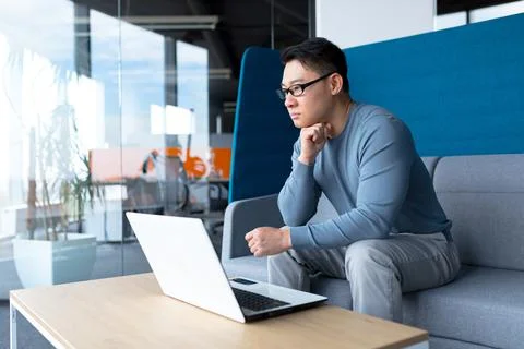Pensive businessman in modern office working on laptop asian boss makes diffi 写真素材