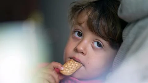 Pensive child eating cookie while laid down on couch, close-up face of smal.. Stock Photos