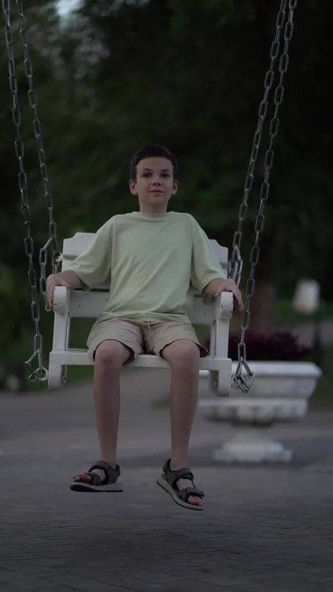 Pensive child rests on playground swing chains during quiet summer evening Stock Footage 340670560