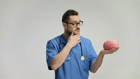 Pensive doctor looking at a brain model 스톡 동영상 77753173