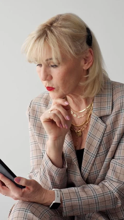 Pensive elderly lady reads smartphone updates attentively in neutral studio Vídeo Stock 346491202