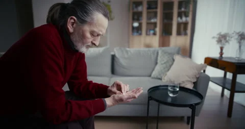 Pensive elderly man sitting alone on sofa in a quiet living room at home Vidéo 336288625