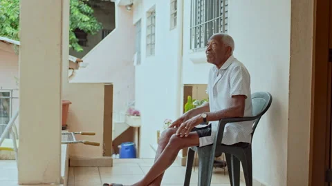 Pensive Elderly Man Sitting On Balcony Looking Up Surrounded By Plants And Subur Stock Footage 319778301