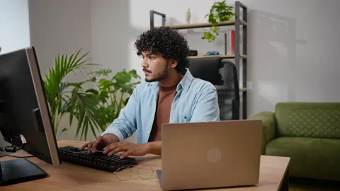 Pensive Hindus programmer works on computer sitting at desk Stock Footage 239323094