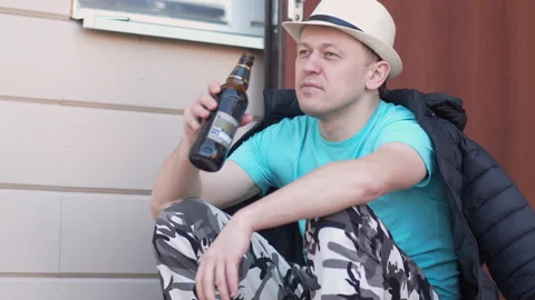 Pensive man with a bottle of beer sits on the doorstep of the house Stock Footage 154011295
