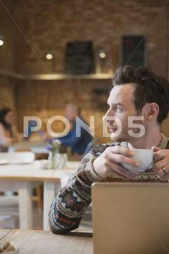 Pensive man looking away drinking coffee at laptop in cafe Stock Photos