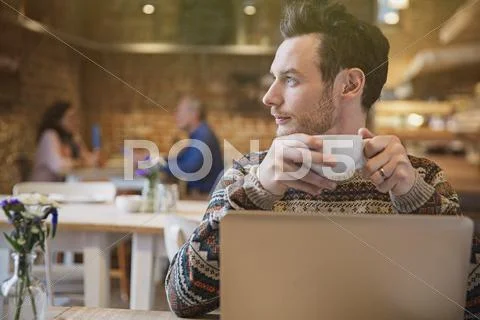 Pensive man looking away drinking coffee at laptop in cafe Stock Photos