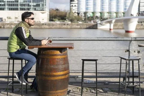 A pensive man looking away while sitting at a bar near the river Stock Photos