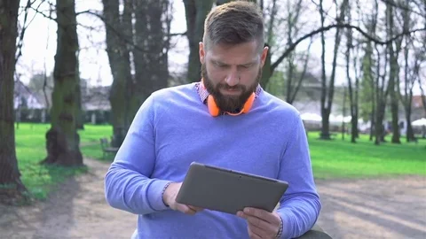 Pensive man in park, browsing tablet computer, portrait steadycam shot 库存影片 74233228