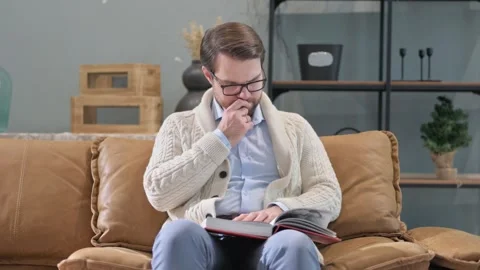 Pensive Man Reading Book while Sitting on Sofa Видео 297449325