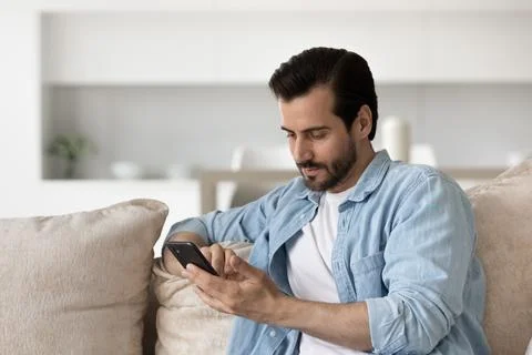 Pensive man relax on sofa using smartphone Stock Photos