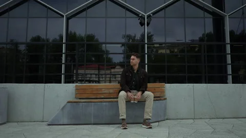 Pensive man sitting on bench, holding two coffee cups, lost in thought Stock Footage 296583334