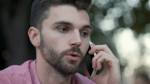 Pensive man sitting outdoor and having a conversation on cellphone Stock Footage