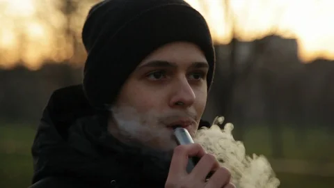 Pensive man smoking electronic cigarette and exhale clounds of vapor in the park Stock Footage 121061840