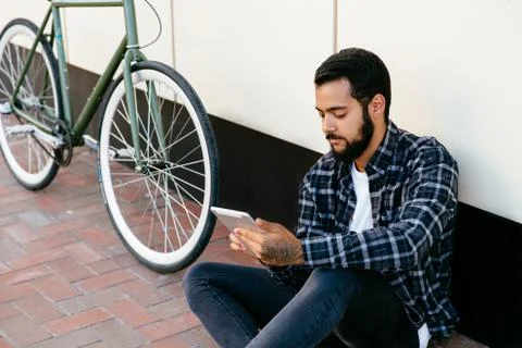 Pensive man using a tablet while sitting near the bike, outdoors. Stock Photos