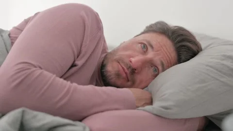 Pensive Middle Aged Man Lying on Side in Bed 動画素材 287409284