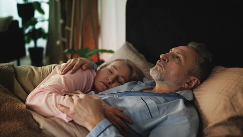 Pensive middle-aged man lying awake in bed and thinking beside his sleeping wife Stock Footage 321615454
