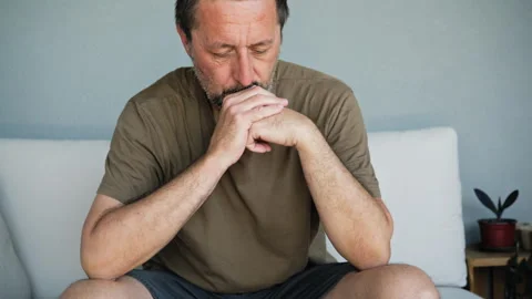 Pensive middle-aged man sitting on sofa deep in thought looking worried and.. Vídeo Stock 346808532