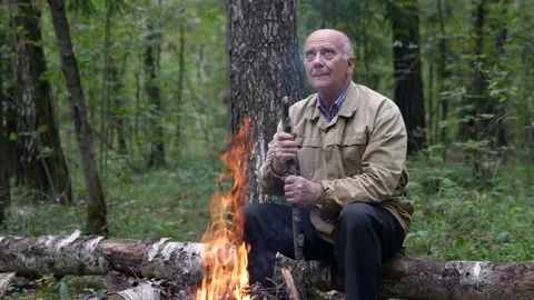 A pensive old traveler is sitting alone in the forest next to a campfire and 스톡 동영상 168646953
