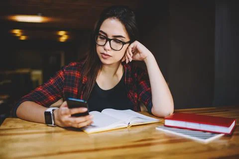 Pensive remote worker with notebooks browsing smartphone in cafeteria Stock Photos