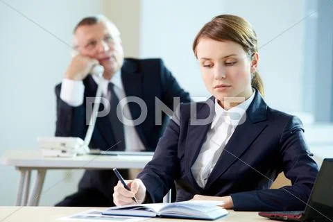 Pensive secretary writing plan of work at workplace Stock Photos