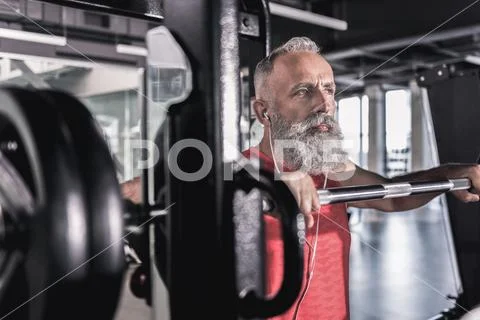 Pensive serious male with beard enjoying workout in athletic center Stock Photos