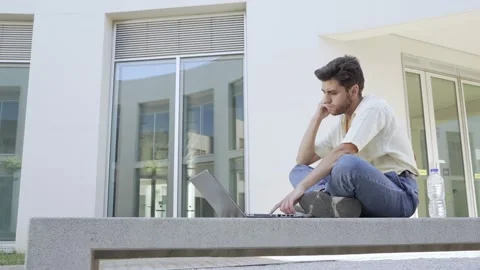 Pensive student while typing on his laptop in the university yard Stock Footage 172040505