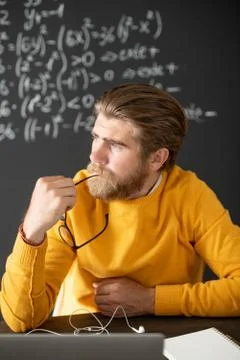 Pensive teacher in yellow pullover thinking of new lecture in front of laptop Stock Photos