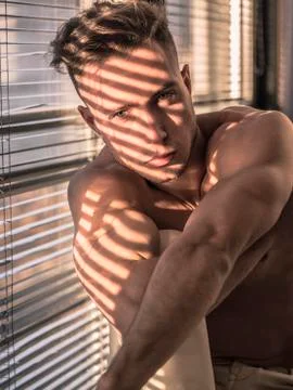 Pensive topless man in shadow stripes from window Stock Photos