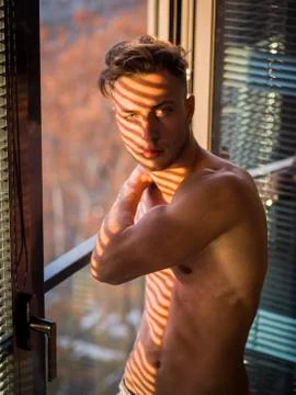 Pensive topless man in shadow stripes from window Stock Photos