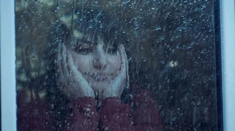 Pensive woman behind window in a rainy day. Shot in slowmotion Stock Footage