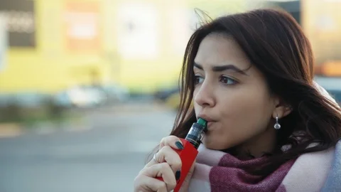 Pensive woman vaping e-cigarette between  cars on the parking zone near the Stock Footage 121482955