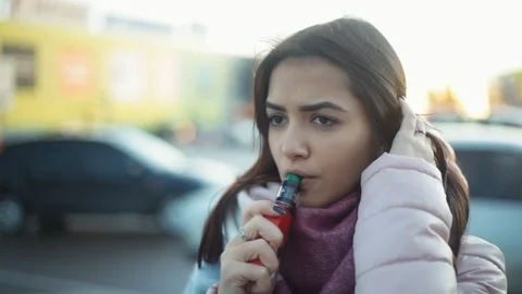 Pensive woman vaping e-cigarette between  cars on the parking zone near the Stock Footage 121482973
