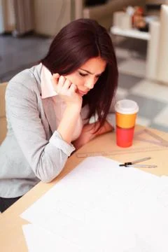Pensive young architect having a problem with her technical drawings Stock Photos
