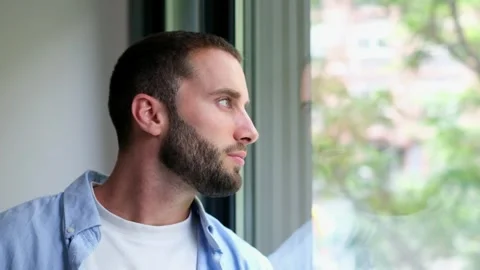 Pensive young bearded man looking out window Stock Footage 335588136