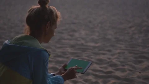 Pensive young girl using a tablet and sitting on the beach at sunset. Chromakey. Stock Footage 83672214