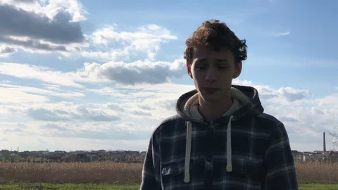 Pensive young guy with short curly hair standing on the blue cloudy sky Stock Footage 106637239