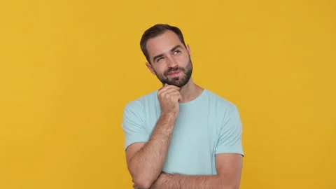 Pensive young man 20s in basic casual blue t-shirt looking camera around with Video stock 148282893
