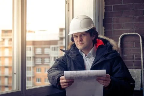 Pensive young man builder in hard hat standng and thinking. Soft focus, toned. Stock Photos